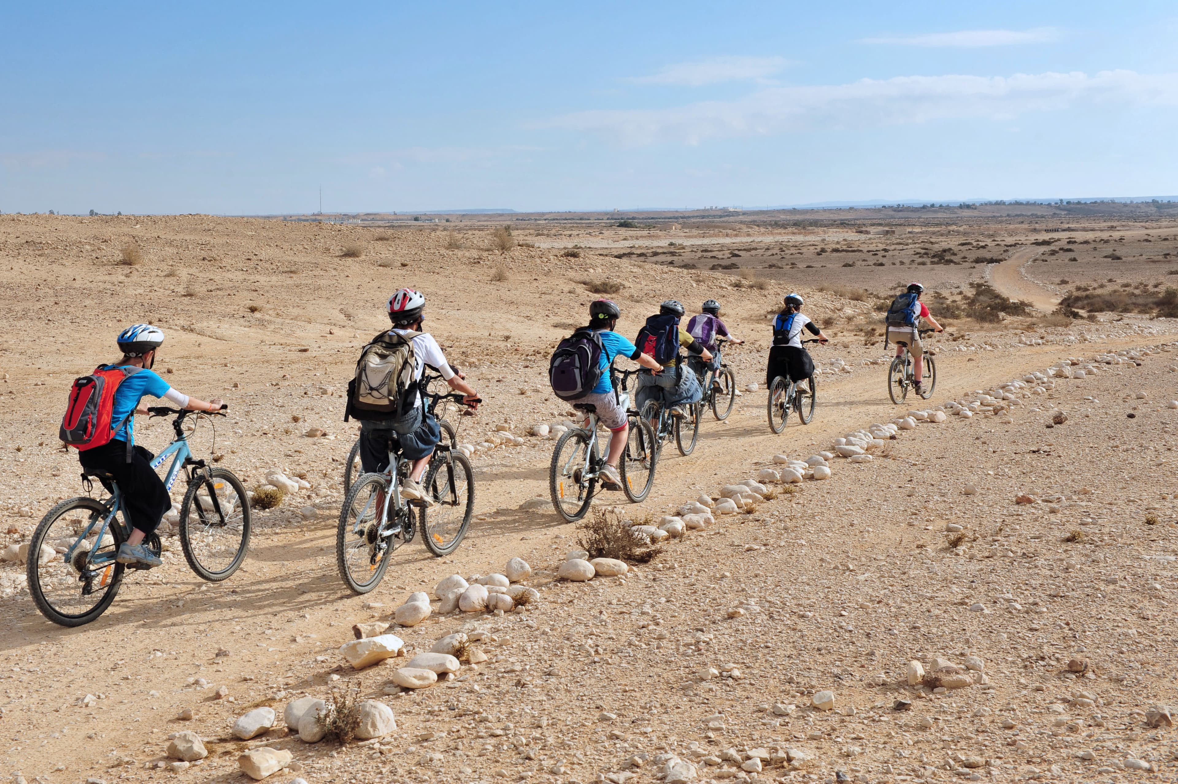 A group of cyclists biking through a desert trail with backpacks and helmets under a clear sky.