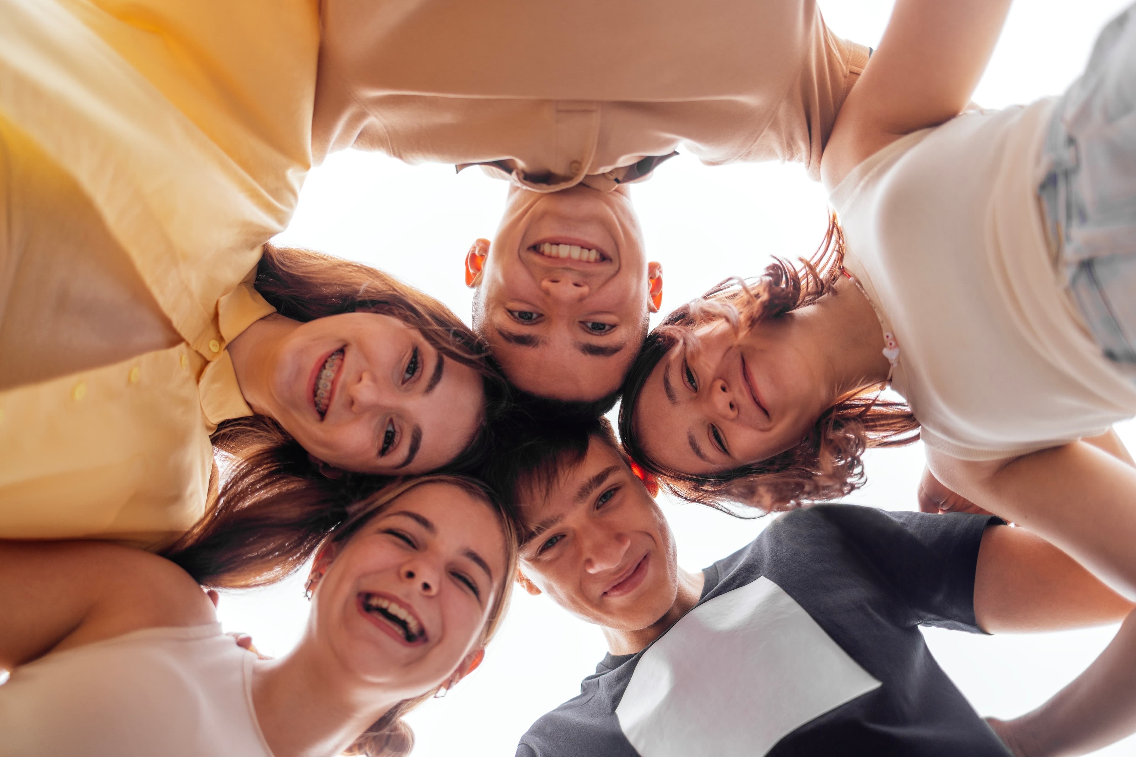 A group of cheerful young friends huddled together in a circle, smiling and looking down at the camera